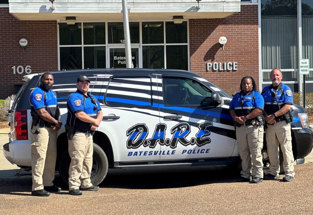 Four resource officers standing in front of D.A.R.E vehicle